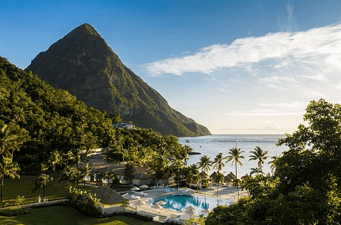 Beautiful view of the Piton Mountains in St. Lucia from a resort with a serene pool and beach with palm trees.