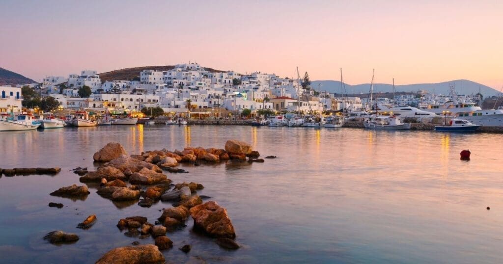 Sunset view of the historic harbor in Naoussa, Paros, featuring traditional fishing boats and coastal stone walls.