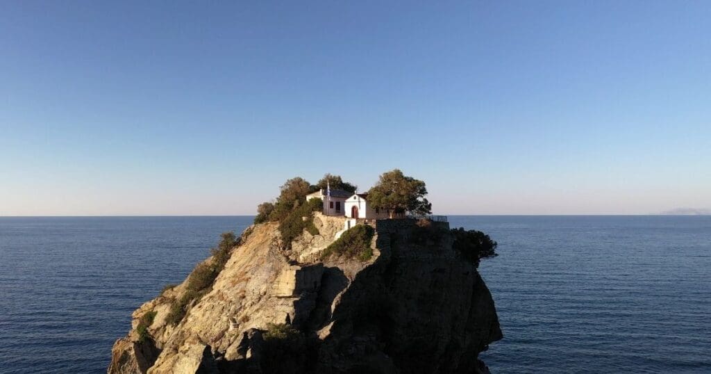 The historic Agios Ioannis Chapel perched dramatically on top of a steep rock formation surrounded by the blue sea in Skopelos, Greece.