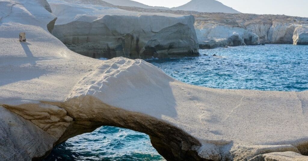 The dramatic white volcanic rock formations and natural stone archway of Sarakiniko Beach against the turquoise sea in Milos, Greece.